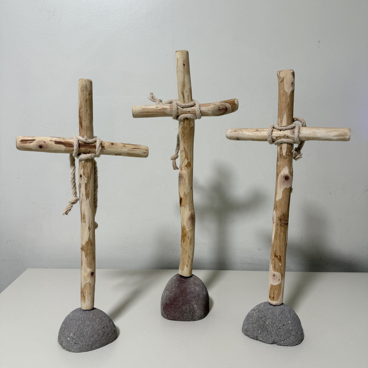 Three rustic wood crosses with rope-wrapped joints standing on stone bases