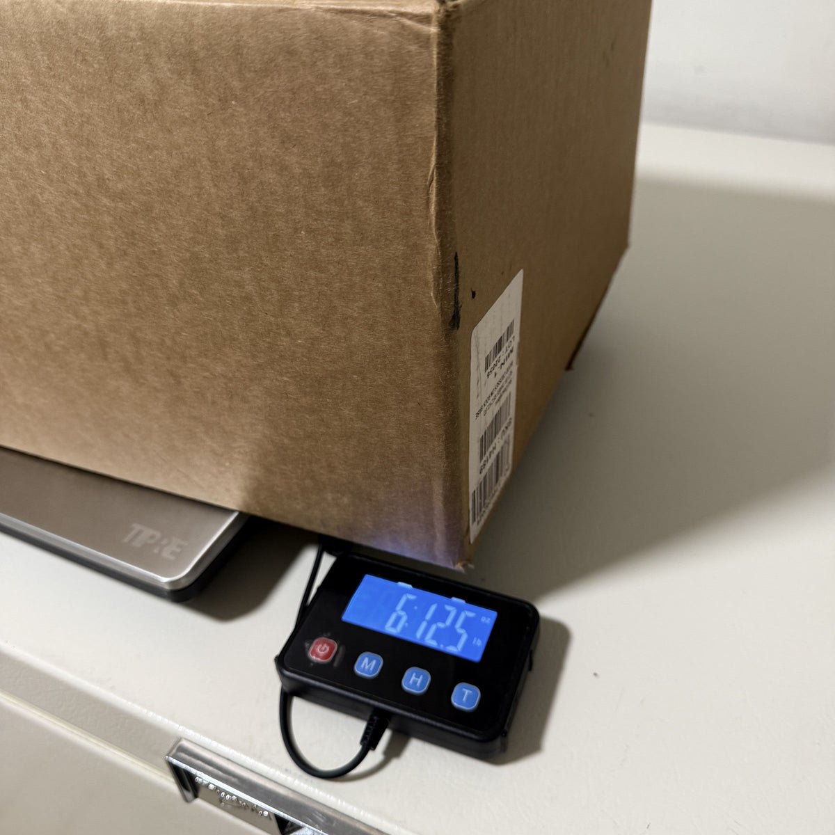 Shipping carton of crosses on a digital scale reading 6 lb 12.5 oz