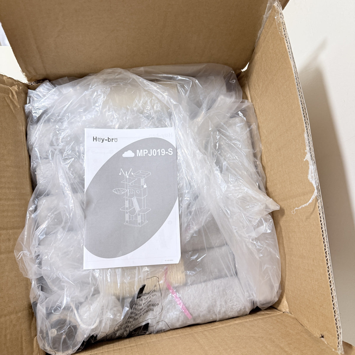 Open Hey-brother cat tree carton showing the bagged parts and the instruction sheet